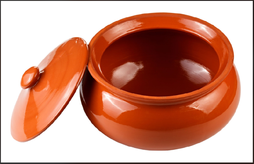 alt="A glossy terracotta clay cooking pot with its lid resting open beside it"